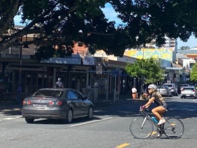 A cyclist rides across a busy road in the Brisbane suburb of West End, with a car passing in the other lane.